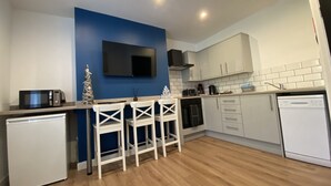 A modern kitchen with a blue accent wall, white cabinets, a built-in oven, a microwave, and a dishwasher. - Blackpool Abode - 20 Bairstow Street (Blackpool)