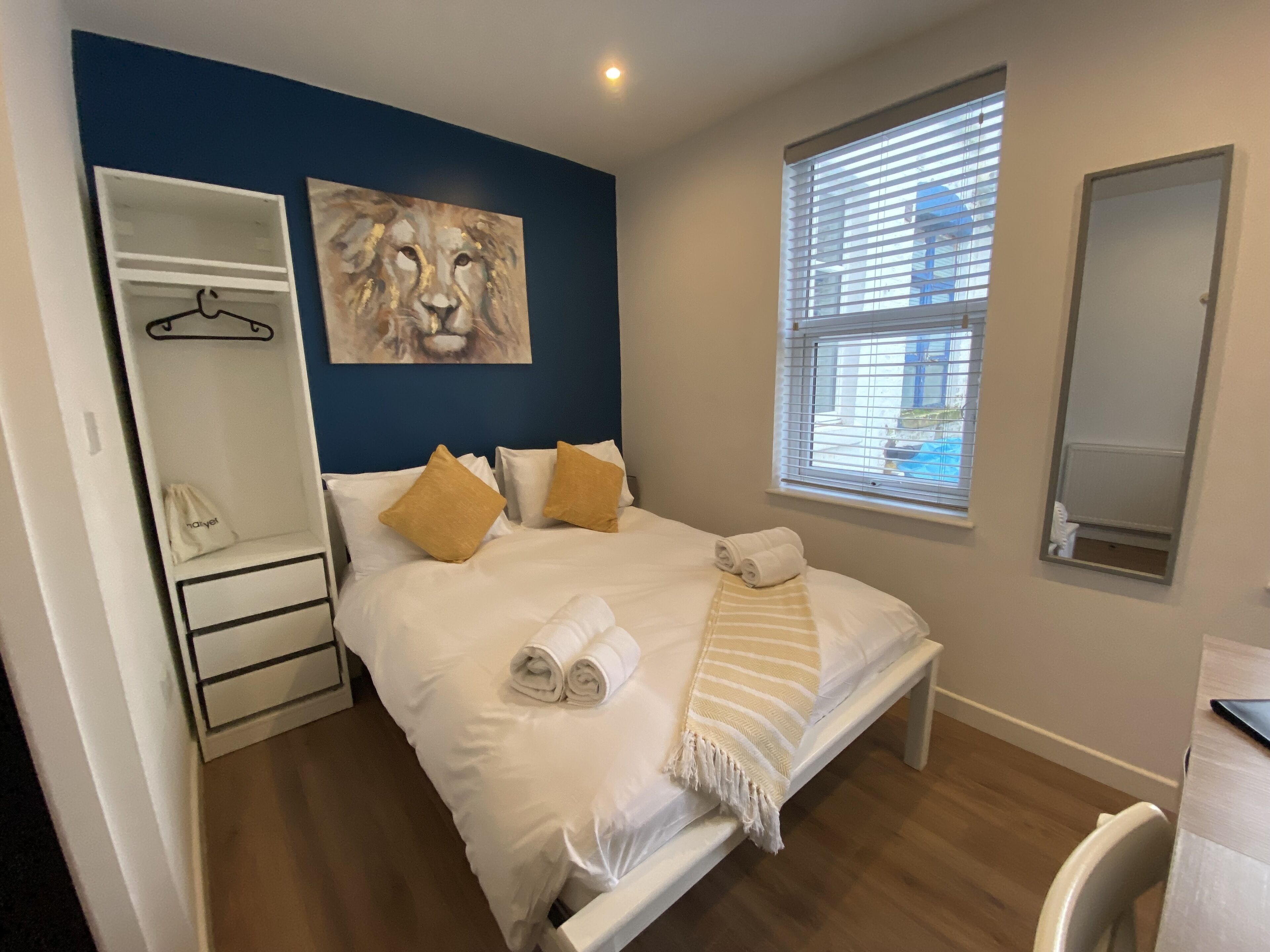 Un dormitorio con cama, armario, espejo y ventana con persianas.