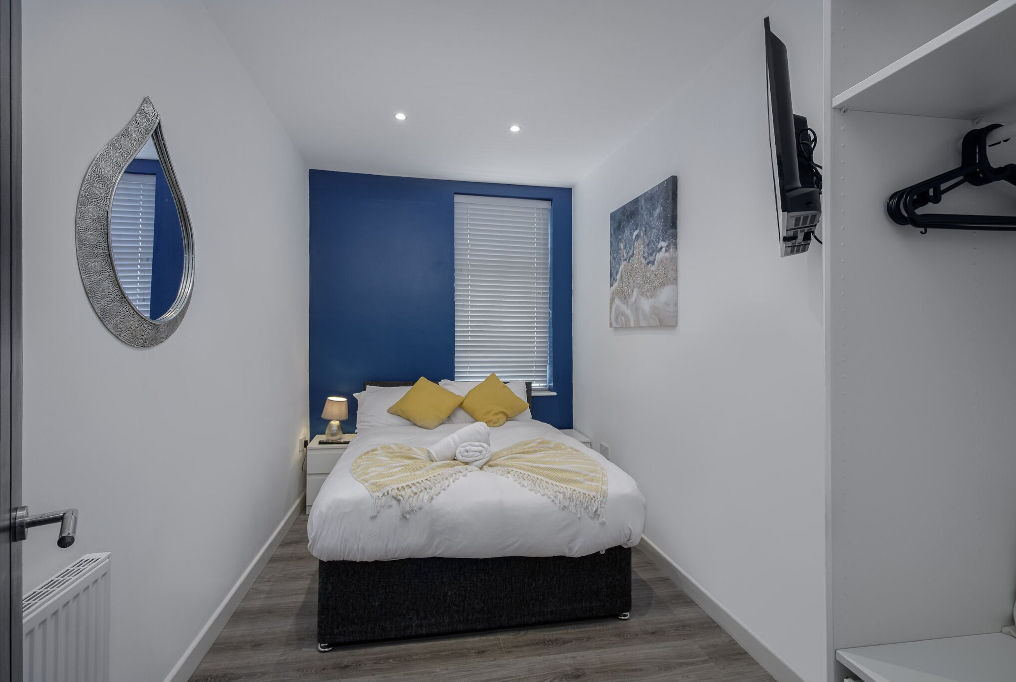 Une chambre à coucher moderne avec un lit, une table de chevet, un miroir et un tableau au mur.