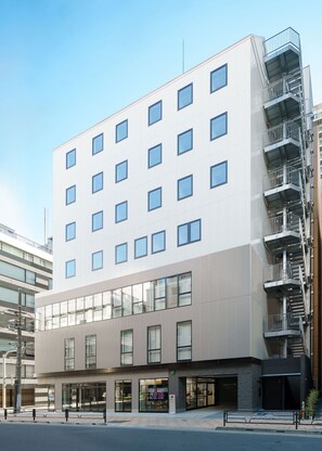 Un hotel moderno a più piani con facciata lineare, ampie finestre e una cascatta di sicurezza ben visibile sul lato destro.