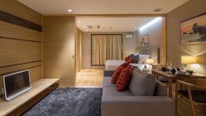 A modern hotel room with a sofa, a TV, a desk with a lamp, and a bed with curtains. - Koharu Resort Hotel & Suites (Hakuba)