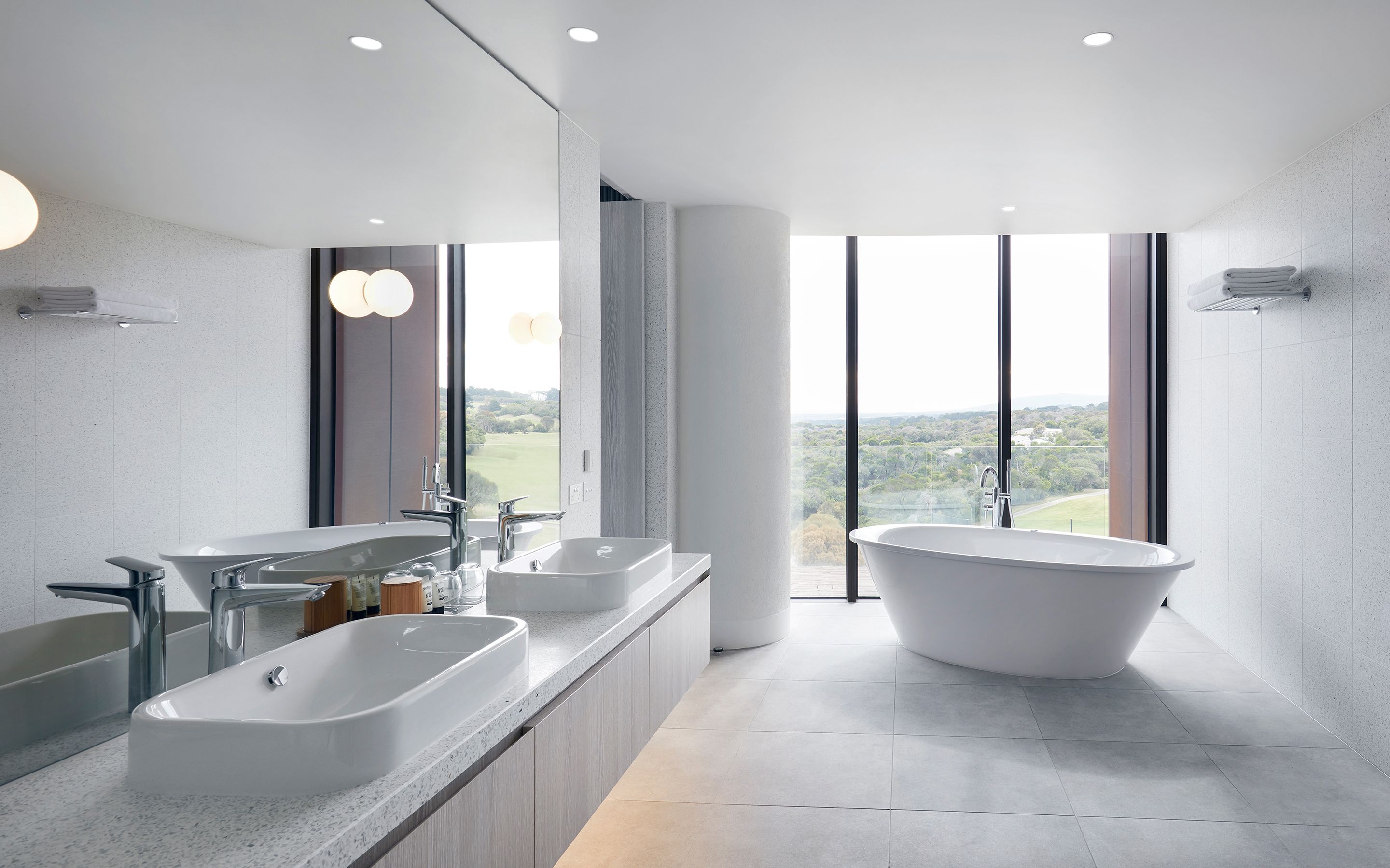 A modern bathroom with a large bathtub, two sinks, and a large window offering a view of a golf course.
