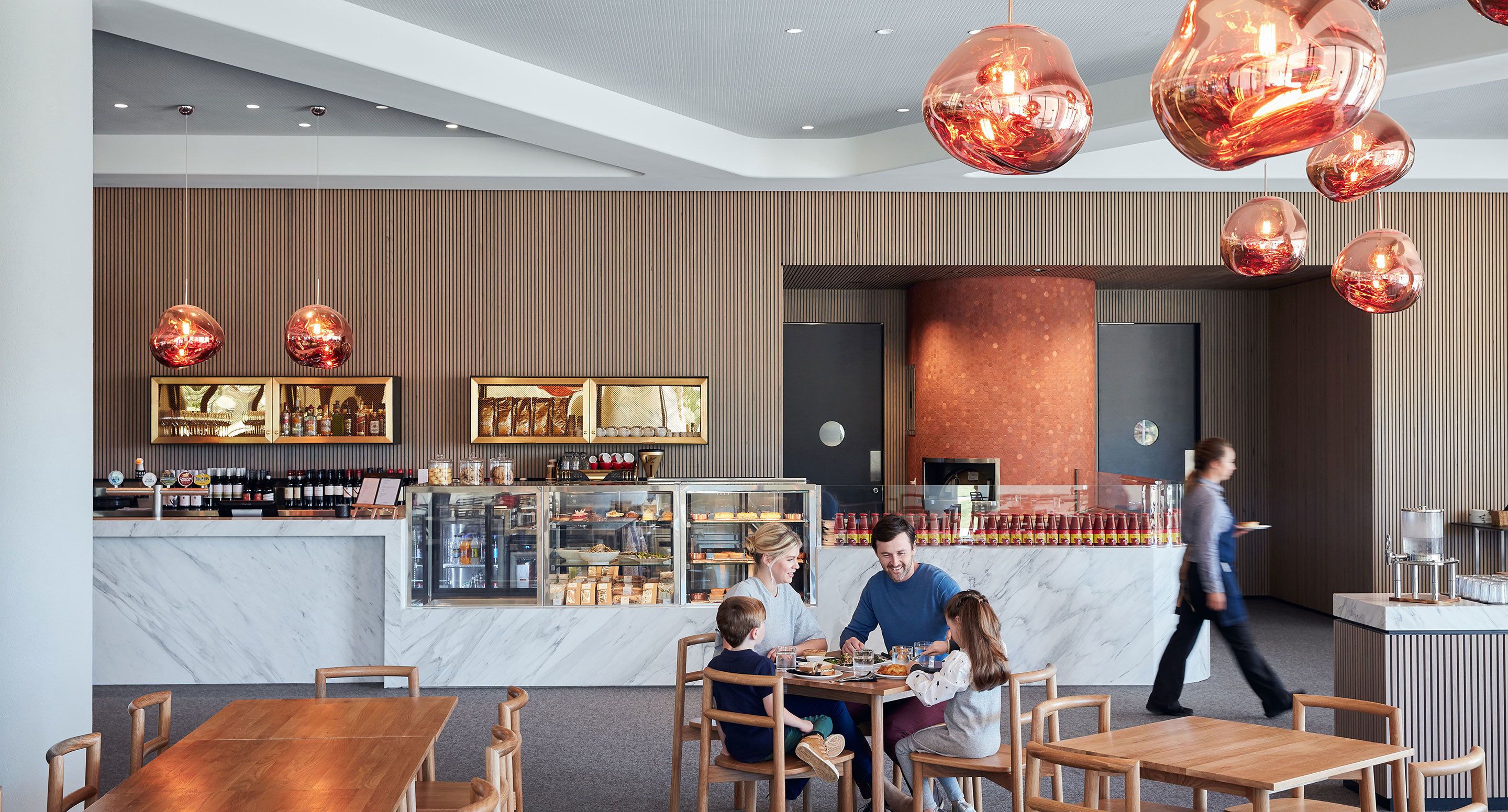 A modern restaurant interior with marble countertops, wooden tables, and hanging spherical light fixtures.