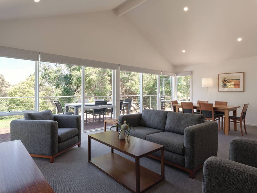 A spacious living area with a large window, a sofa, a coffee table, and a dining table with chairs.