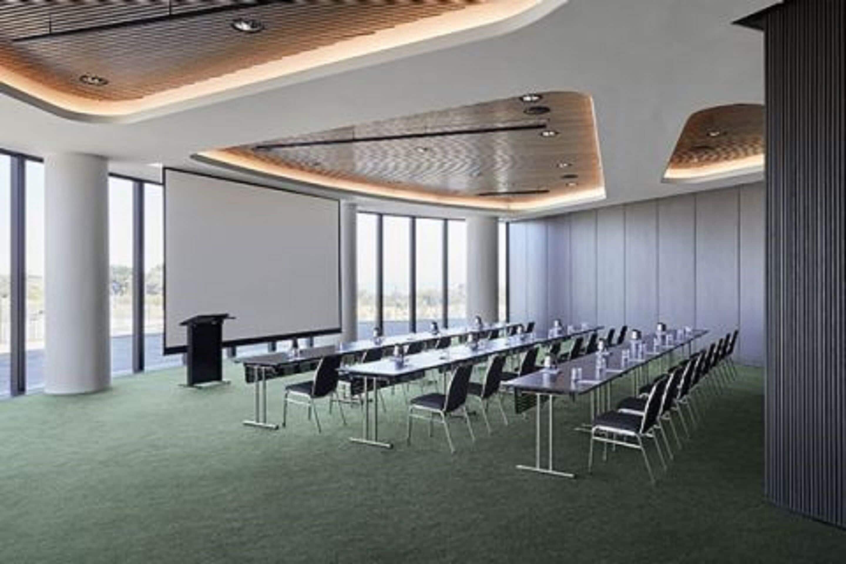 Une salle de conférence moderne, dotée d’une longue table, de chaises, d’un écran de projection et d’une grande fenêtre.