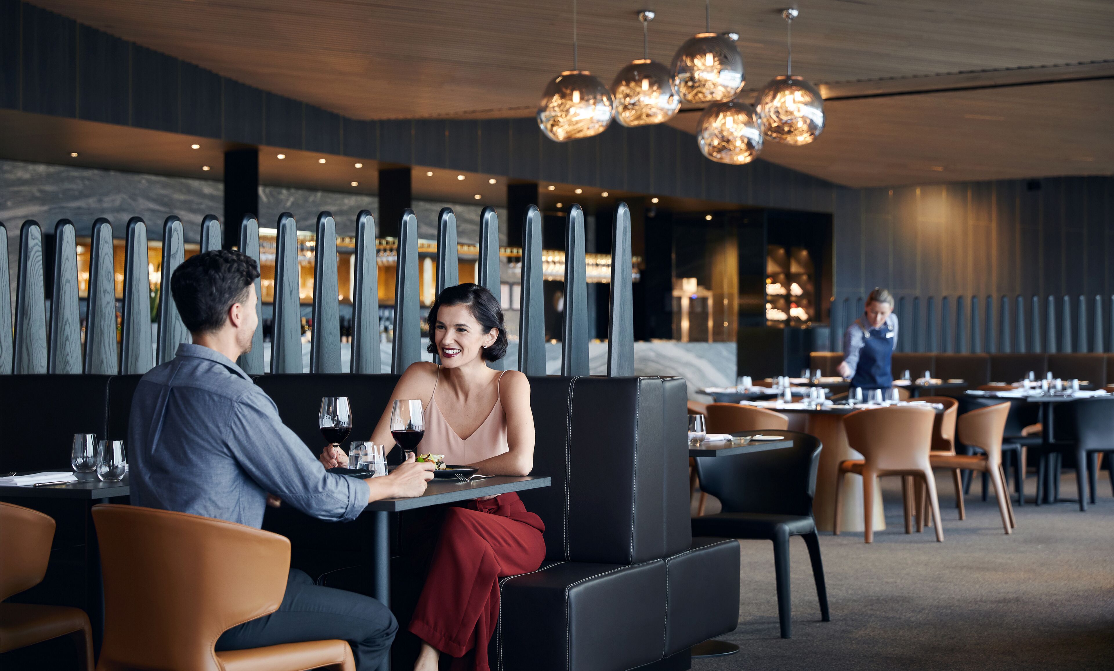 A couple dining at a restaurant with a modern interior, featuring a long counter, cushioned seating, and pendant lighting.