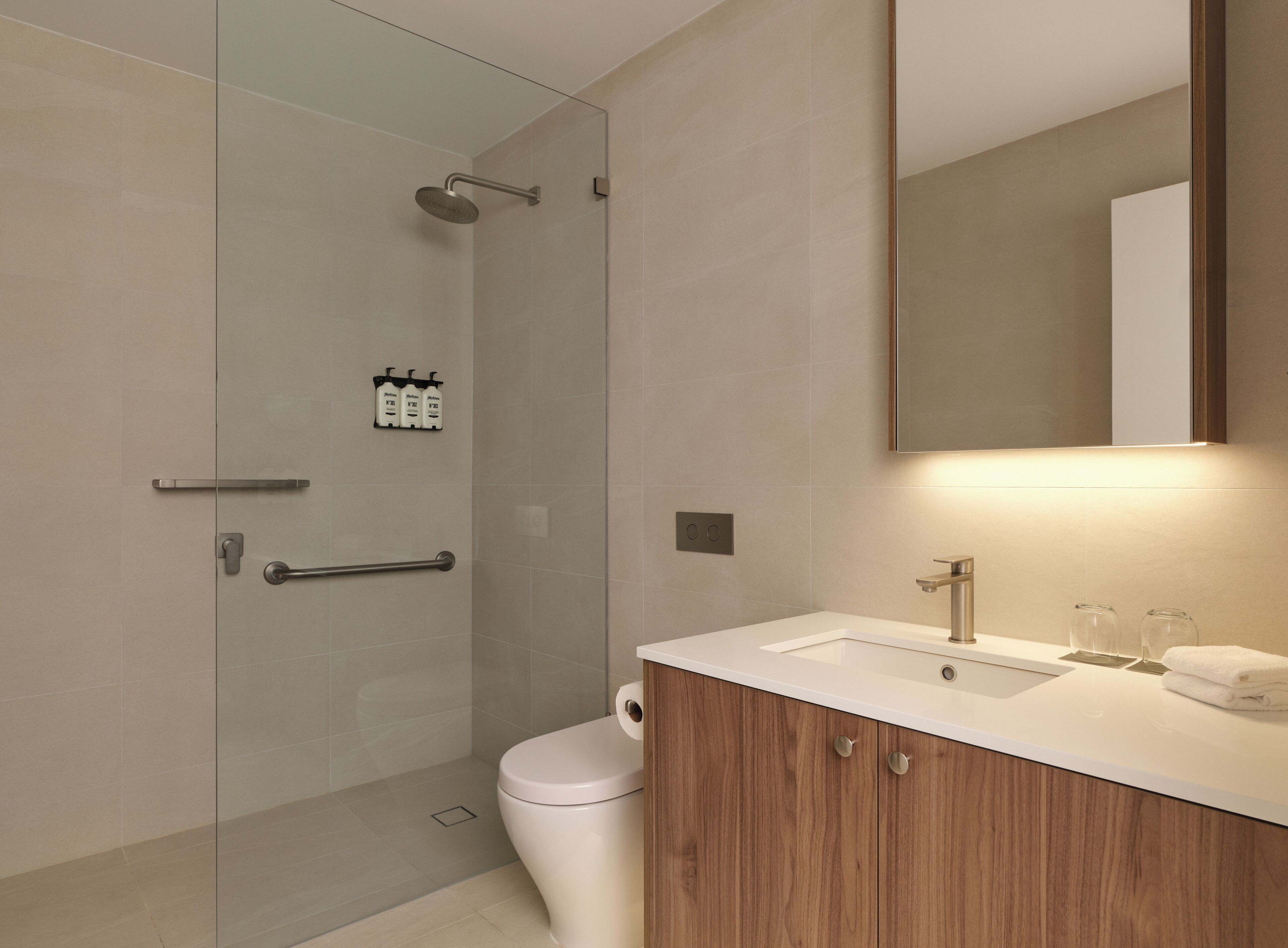 Un baño moderno con cabina de ducha de vidrio, tocador de madera y un espejo grande.