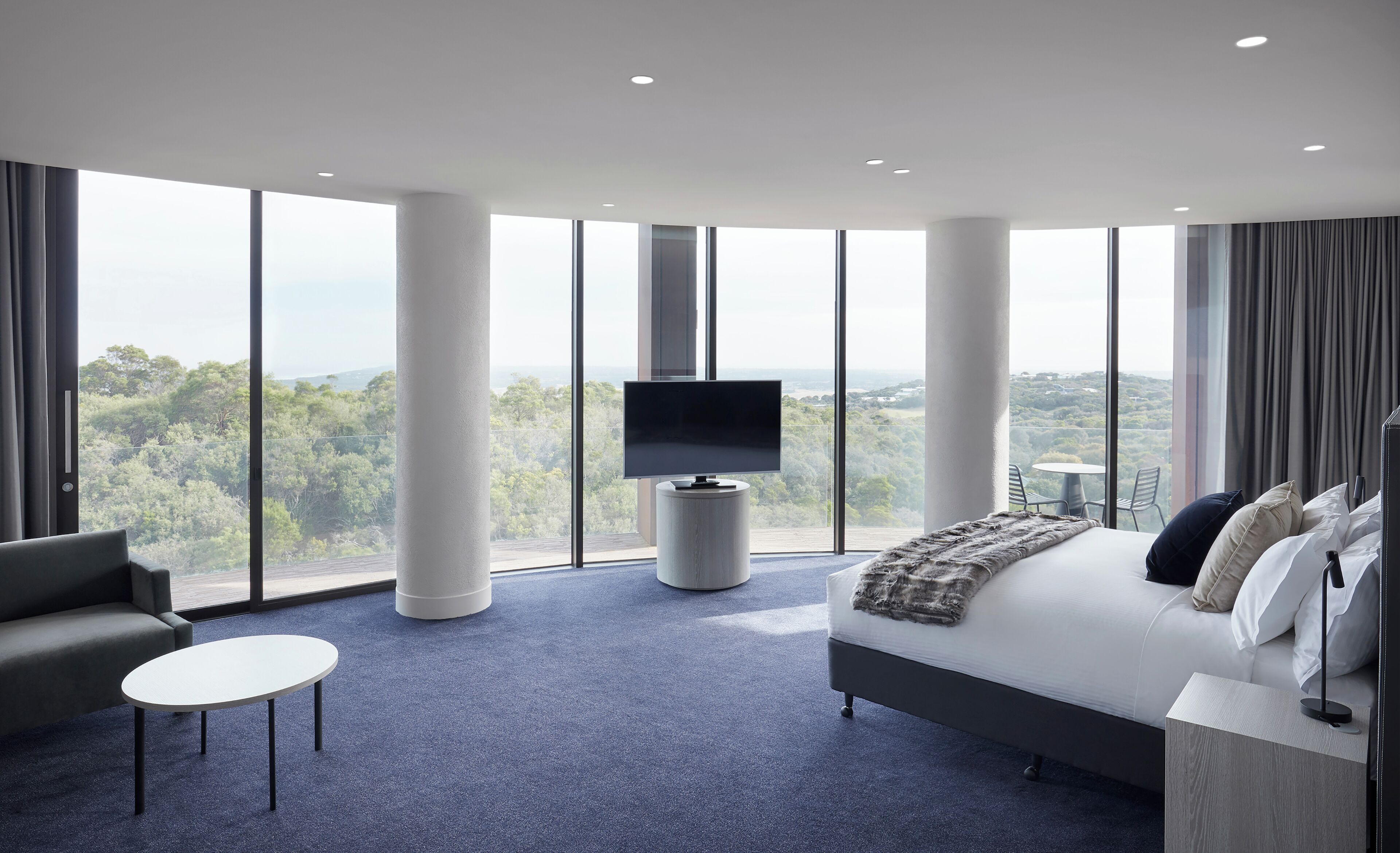 A modern hotel room with a large bed, a TV, a sofa, and a small table.