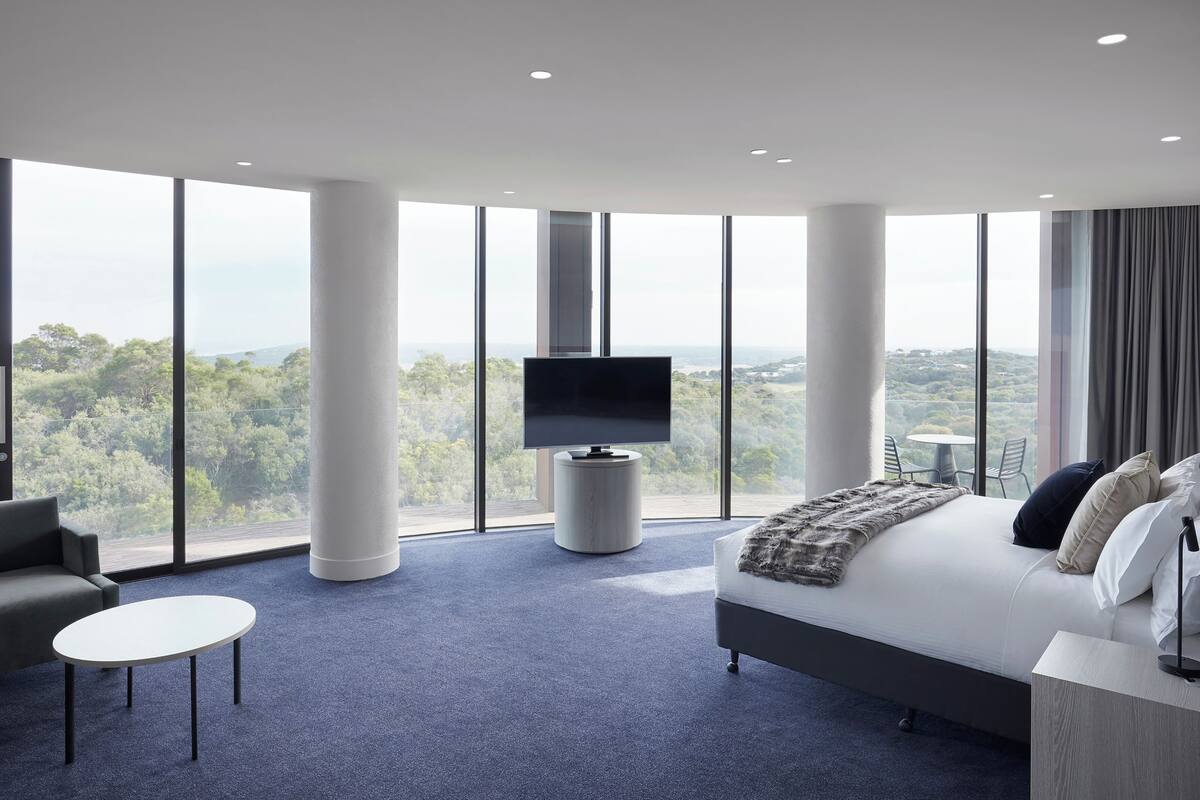 Habitación de hotel moderna con una cama grande, televisor, sofá y una mesita.