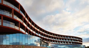 A modern building with a curved facade, multiple balconies, and reflective glass windows.