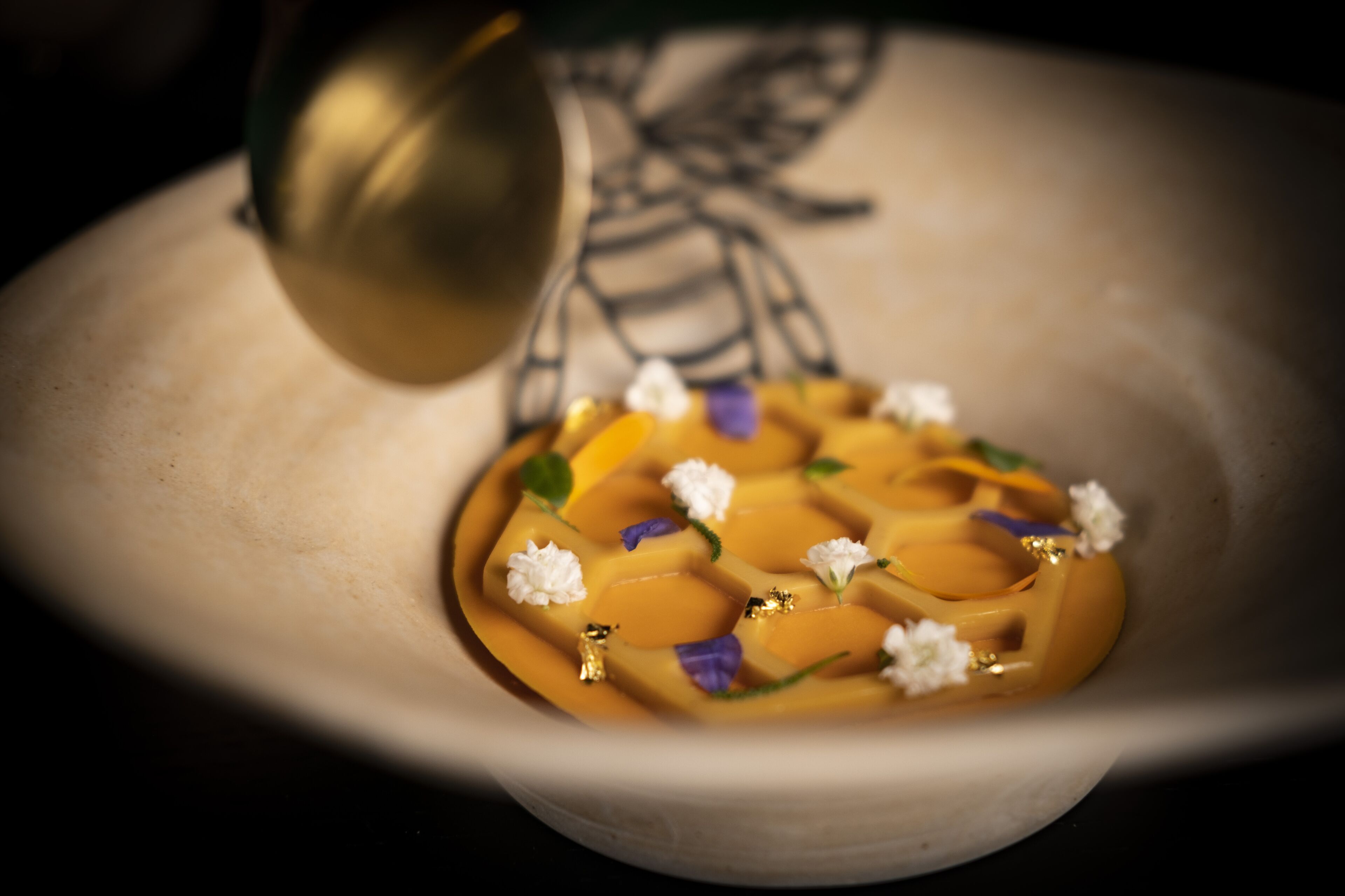 A bowl with a dessert, possibly a panna cotta, garnished with flowers and gold leaf.