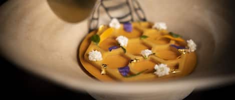 A bowl with a dessert, possibly a panna cotta, garnished with flowers and gold leaf.