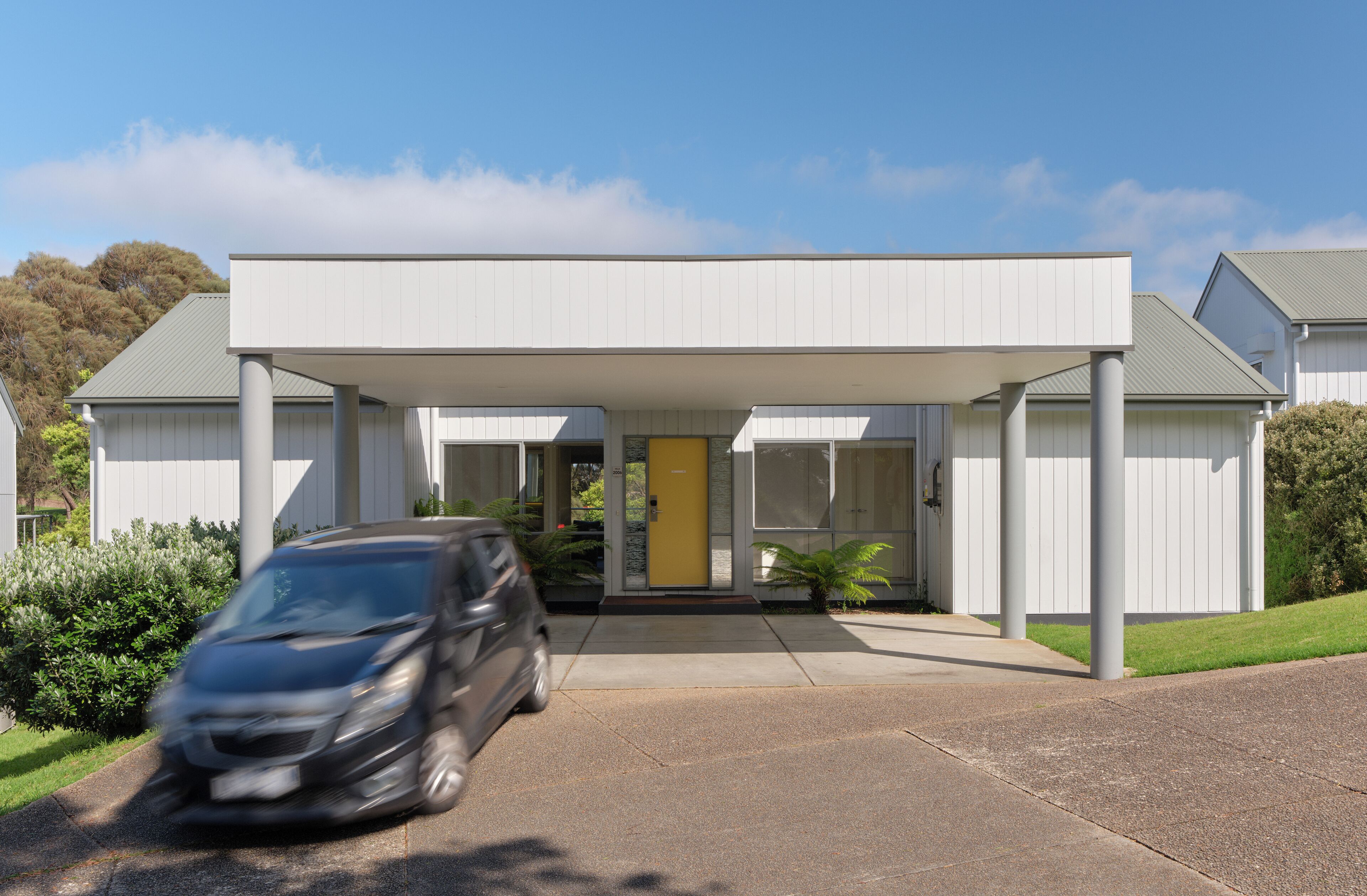 A modern building with a covered entrance, a yellow door, and a car parked in front.