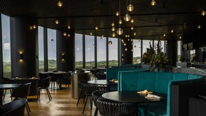 Ein modernes Restaurant mit hohen Decken, schwebenden kugelförmigen Lampen und Blick auf die Landschaft durch große Fenster.