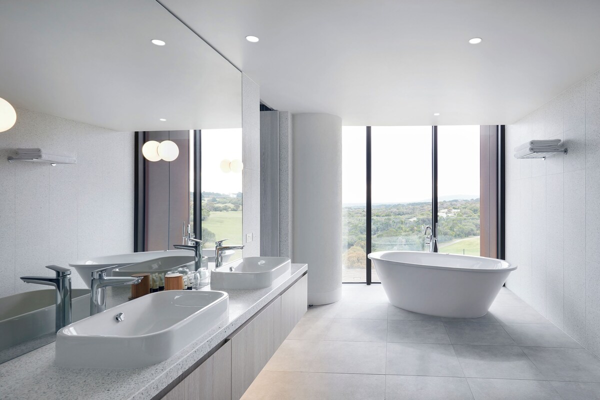 Un baño moderno con una bañera grande, dos lavamanos y un espejo amplio.