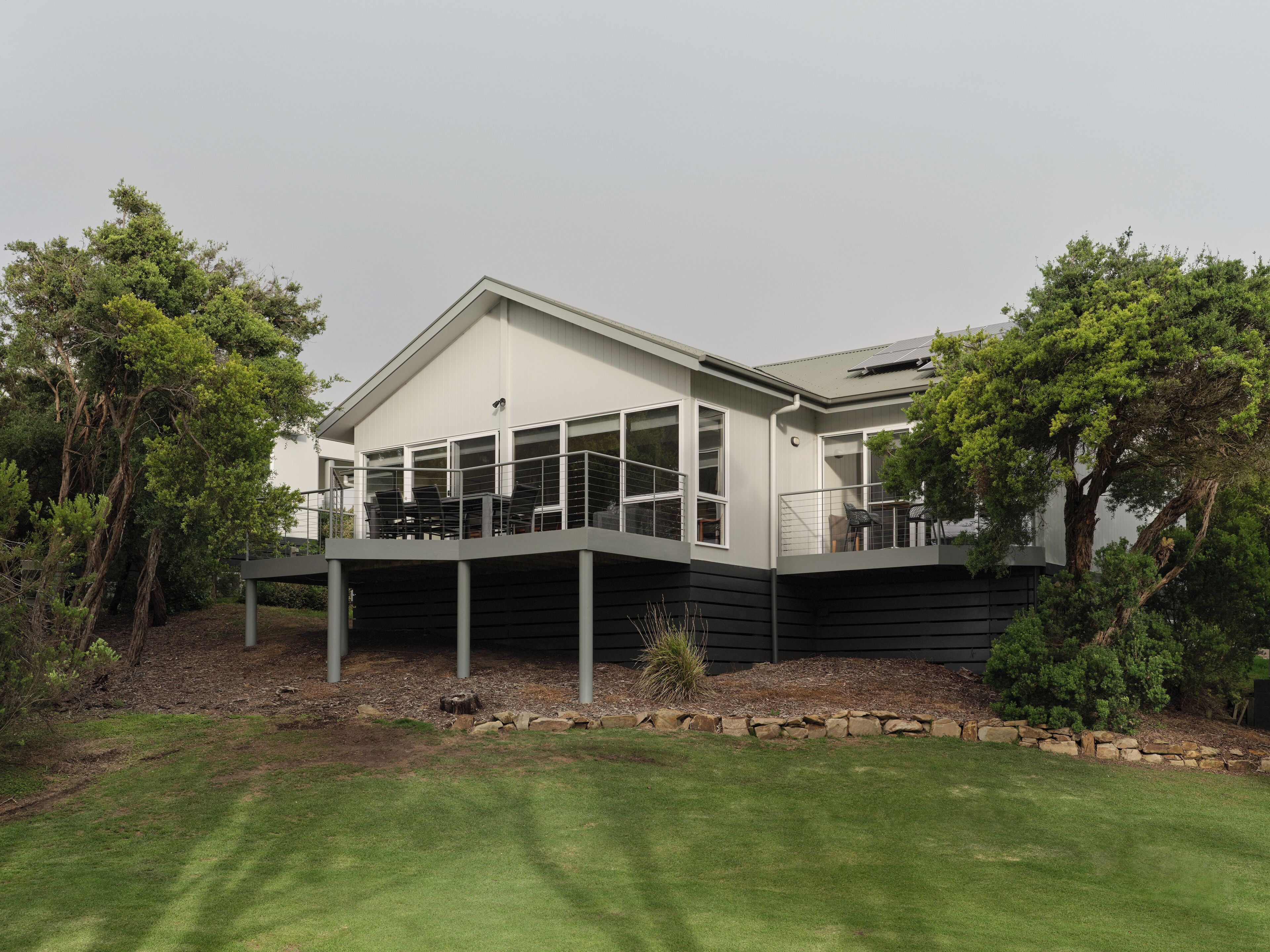 A modern house with a covered patio, large windows, and a stone retaining wall.