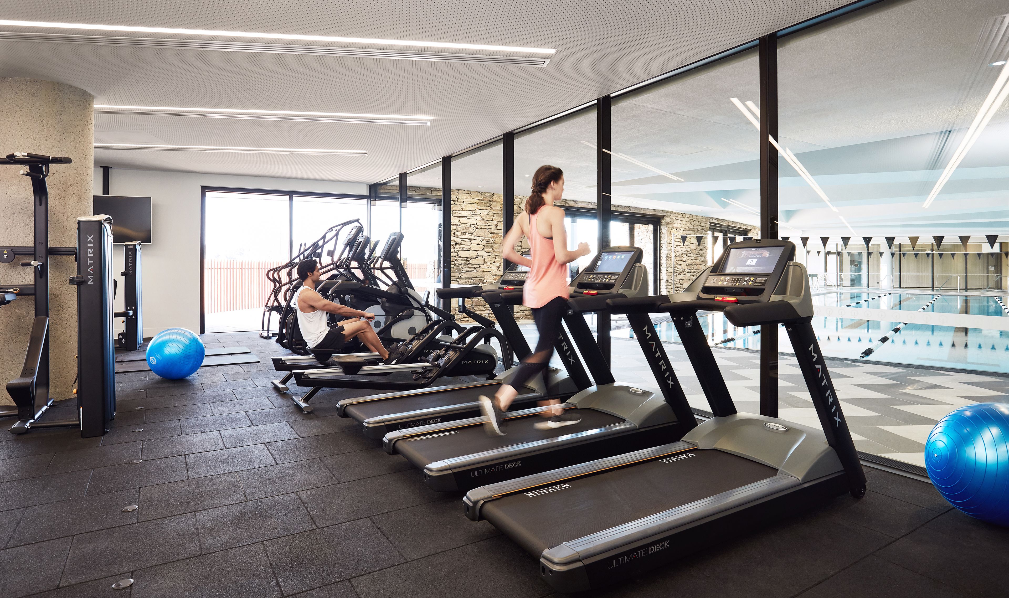 Ein Fitnessstudio mit Laufbändern, Gymbällen und einer Steinwand.