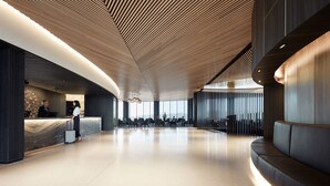 Eine moderne Hotellobby mit einer gebogenen Rezeption, einer Sitzecke und einer hohen Decke mit Holzstruktur.