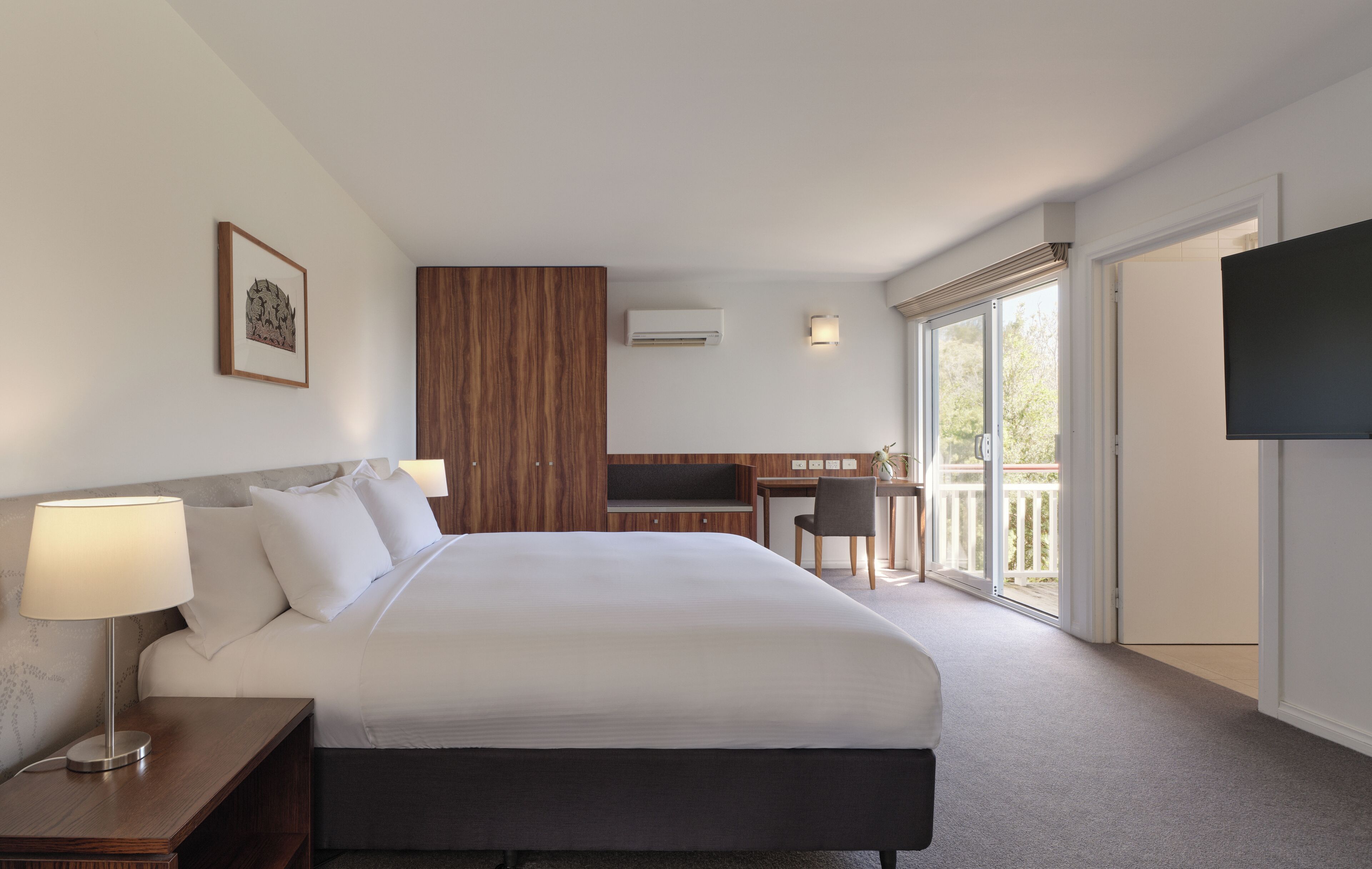 A hotel room with a large bed, a desk, a chair, a TV, and a balcony.