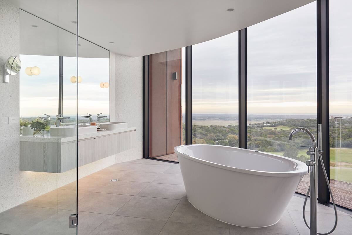 Un baño moderno con una bañera independiente, ducha con mampara de vidrio y un amplio ventanal con vistas a la ciudad.