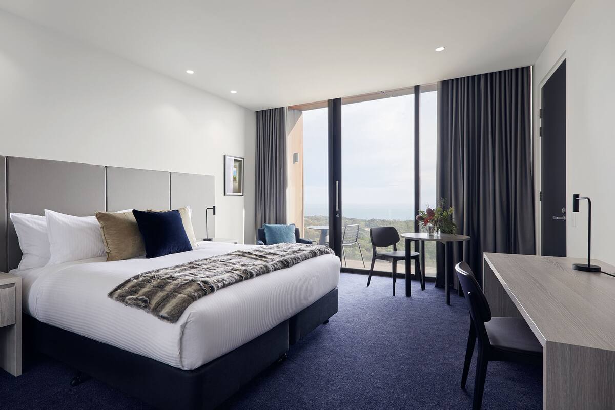 Habitación de hotel moderna con una cama grande, un escritorio, una silla y vistas a la ciudad.