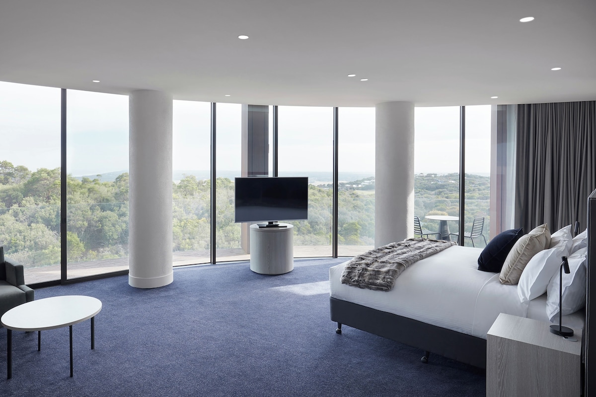 Habitación de hotel moderna con una cama grande, televisor, sofá y una mesita.