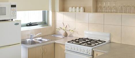 A modern kitchen with a microwave, sink, stove, and a bowl of tomatoes and peppers on the counter.