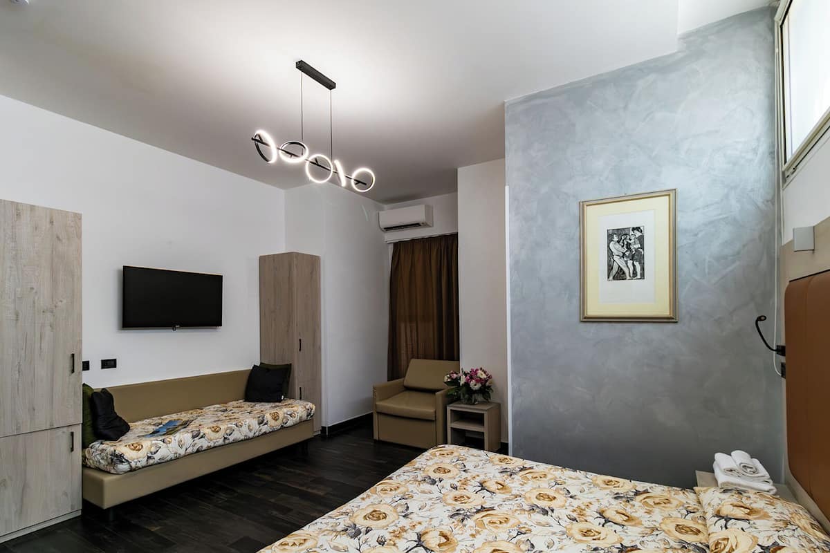 Une chambre d’hôtel moderne équipée d’un lit, d’un canapé-lit, d’une télévision, d’une armoire et d’un tableau encadré au mur.