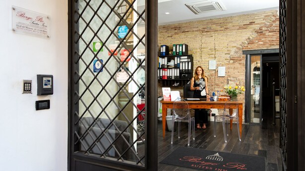 Una recepción con una recepcionista, un muro de ladrillo y una puerta con teclado de seguridad.