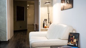 Una sala de estar moderna con un sofá de cuero blanco, una mesita con un libro y una botella, y un cuadro en la pared.