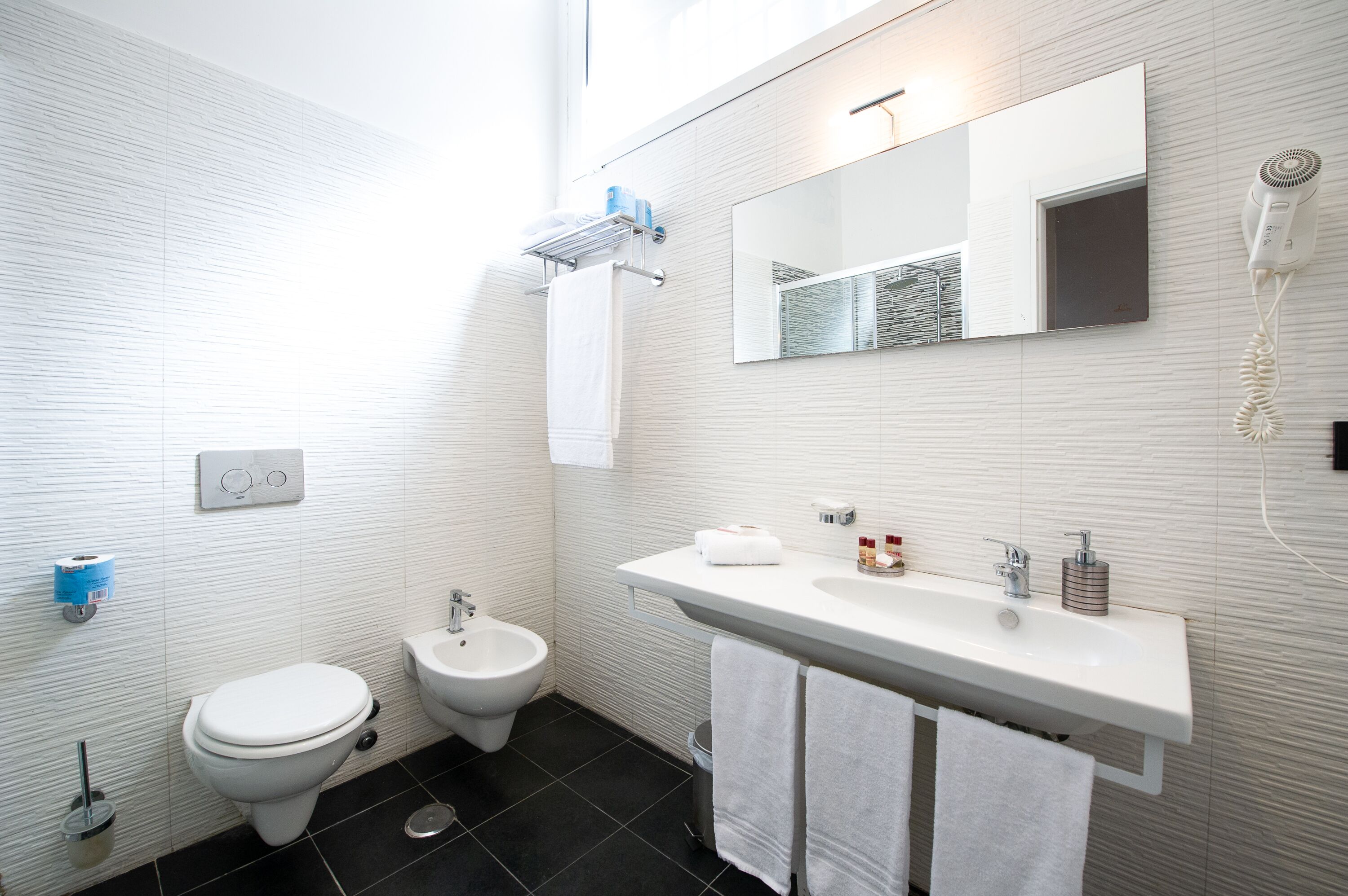 A modern bathroom with a toilet, bidet, sink, and mirror.