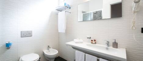 A modern bathroom with a toilet, bidet, sink, and mirror.