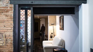 Una sala moderna con un sofá blanco, una mesita y una lámpara de pie. Una persona entra caminando por un umbral hacia otra habitación.