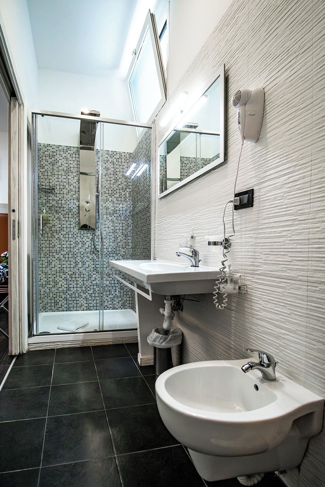 A modern bathroom with a glass-enclosed shower, a white sink, and a bidet.