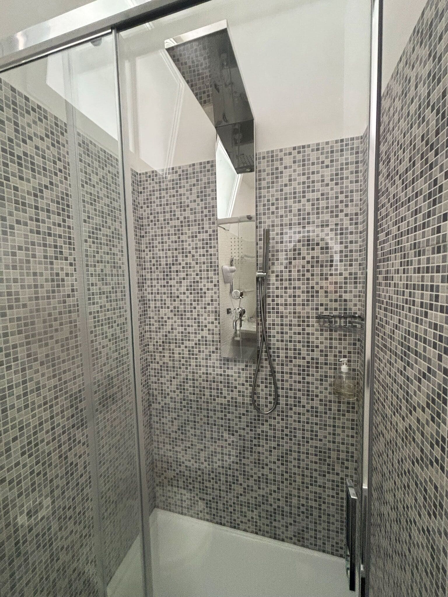A modern bathroom with mosaic tile walls, a glass shower enclosure, and a visible hand dryer.