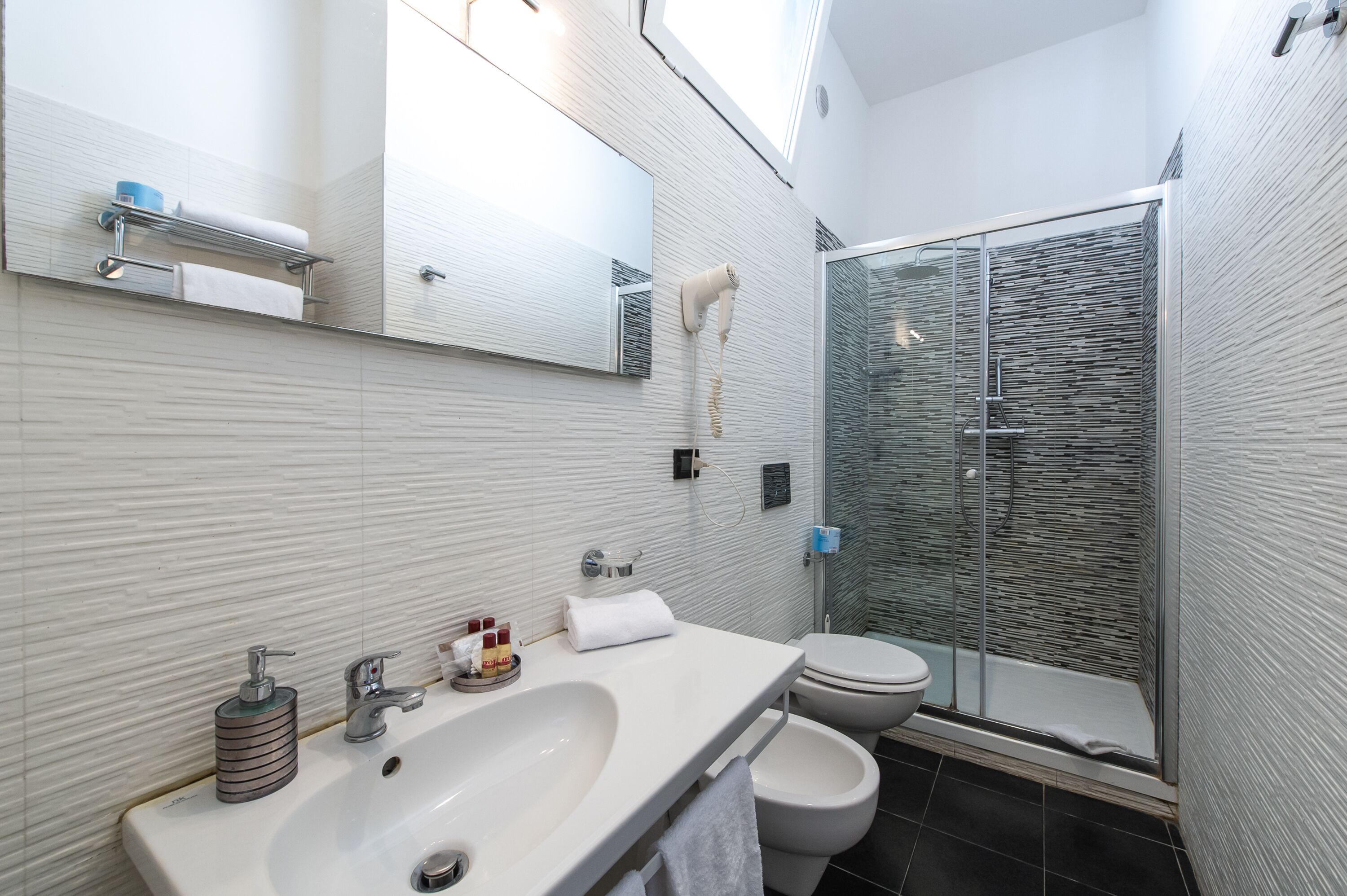 A modern bathroom with a white sink, a mirror, a towel rack, a glass shower enclosure, and a toilet.