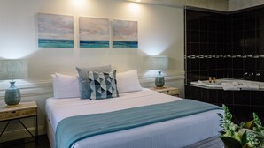 A hotel room with a bed, two wall-mounted paintings, a black tiled shower area, and a small plant. - Fairways Resort (Rosebud)