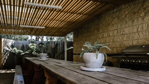 An outdoor patio with a wooden table, a potted plant, and a grill. - Fairways Resort (Rosebud)