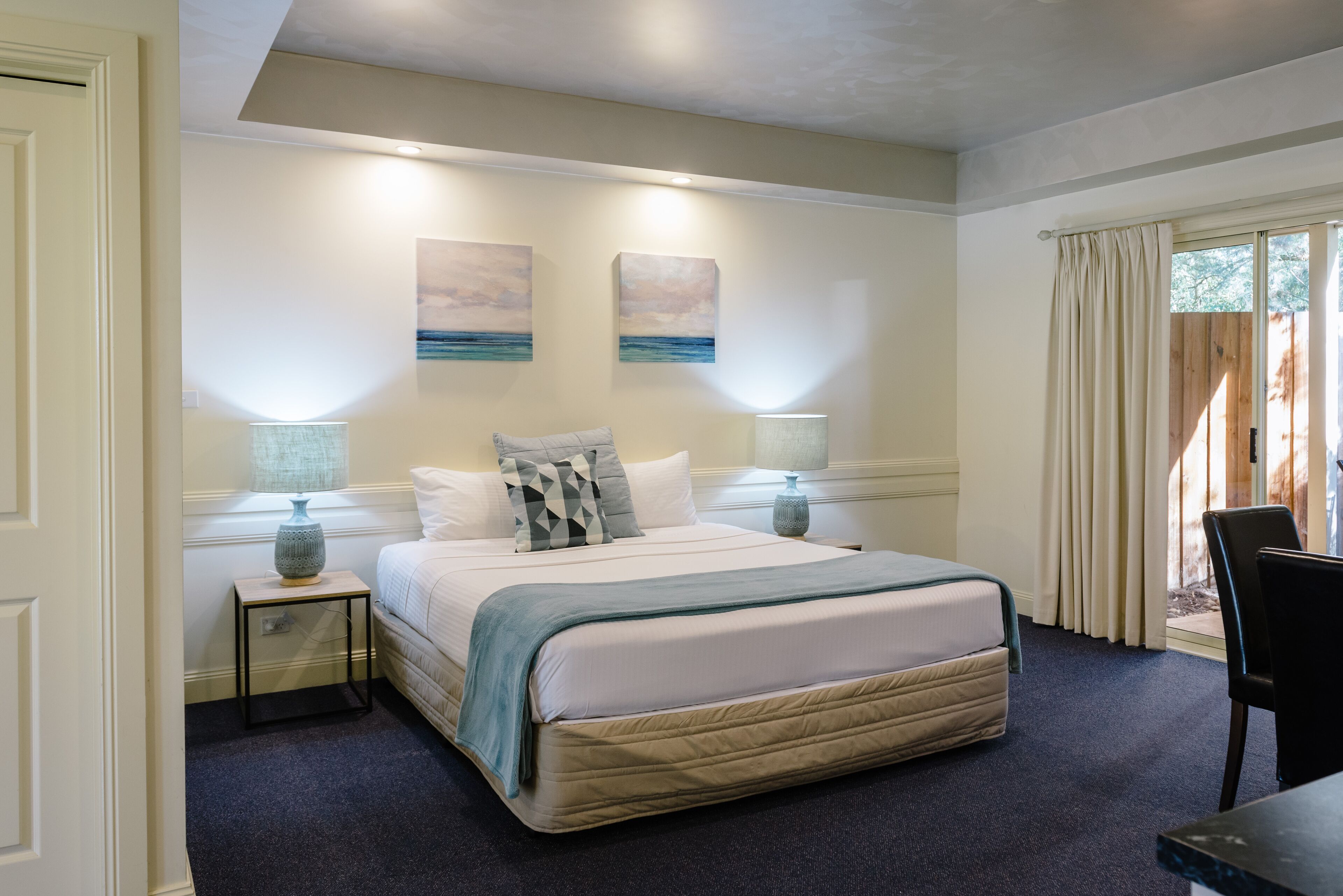 A neatly arranged bedroom with a large bed, two bedside tables with lamps, and artwork on the walls.