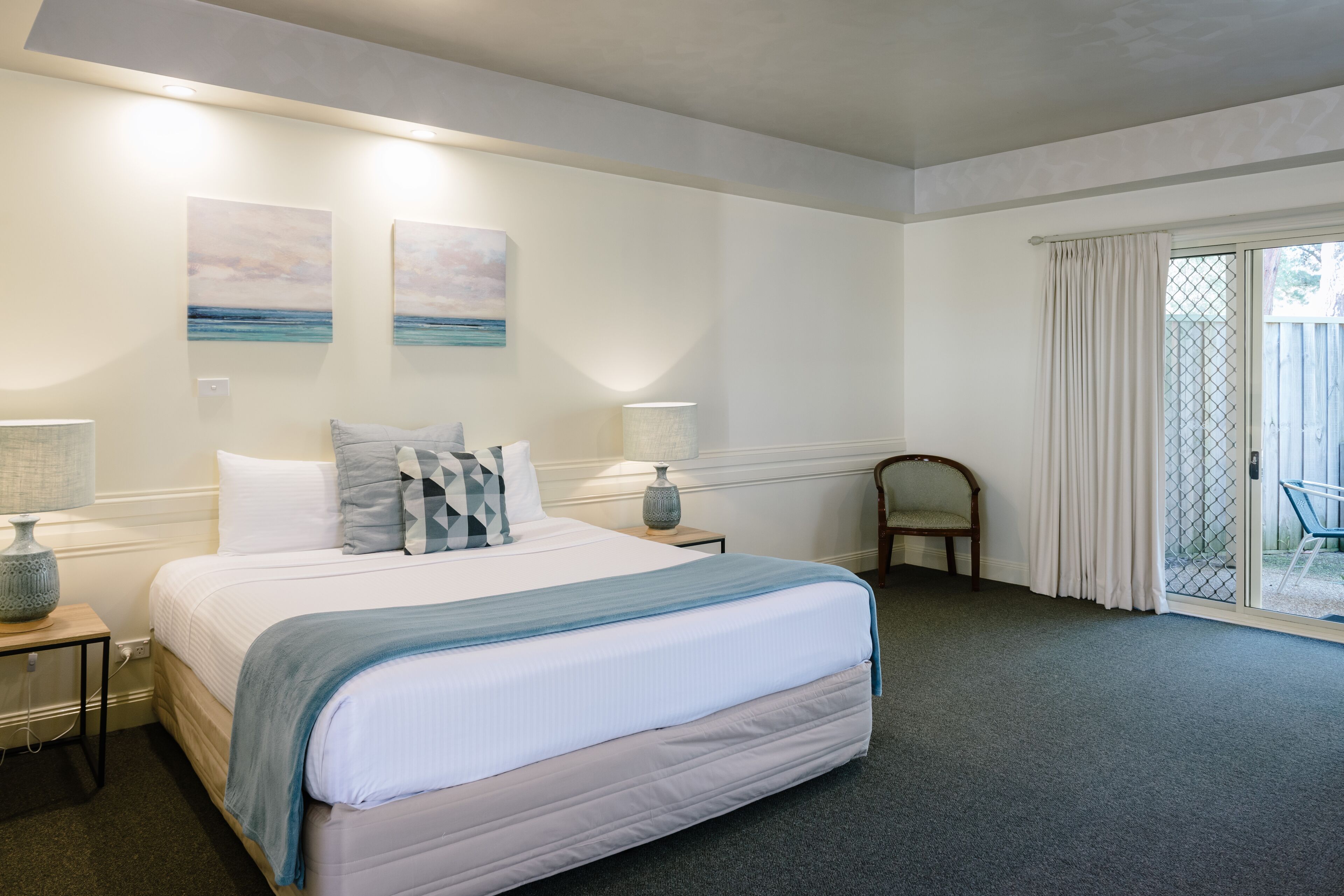 Een slaapkamer met een groot bed, twee wandlampen, een stoel en uitzicht door een schuifdeur.
