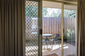 A sliding glass door leading to a patio with a table and two chairs, a wooden fence, and a view of trees.