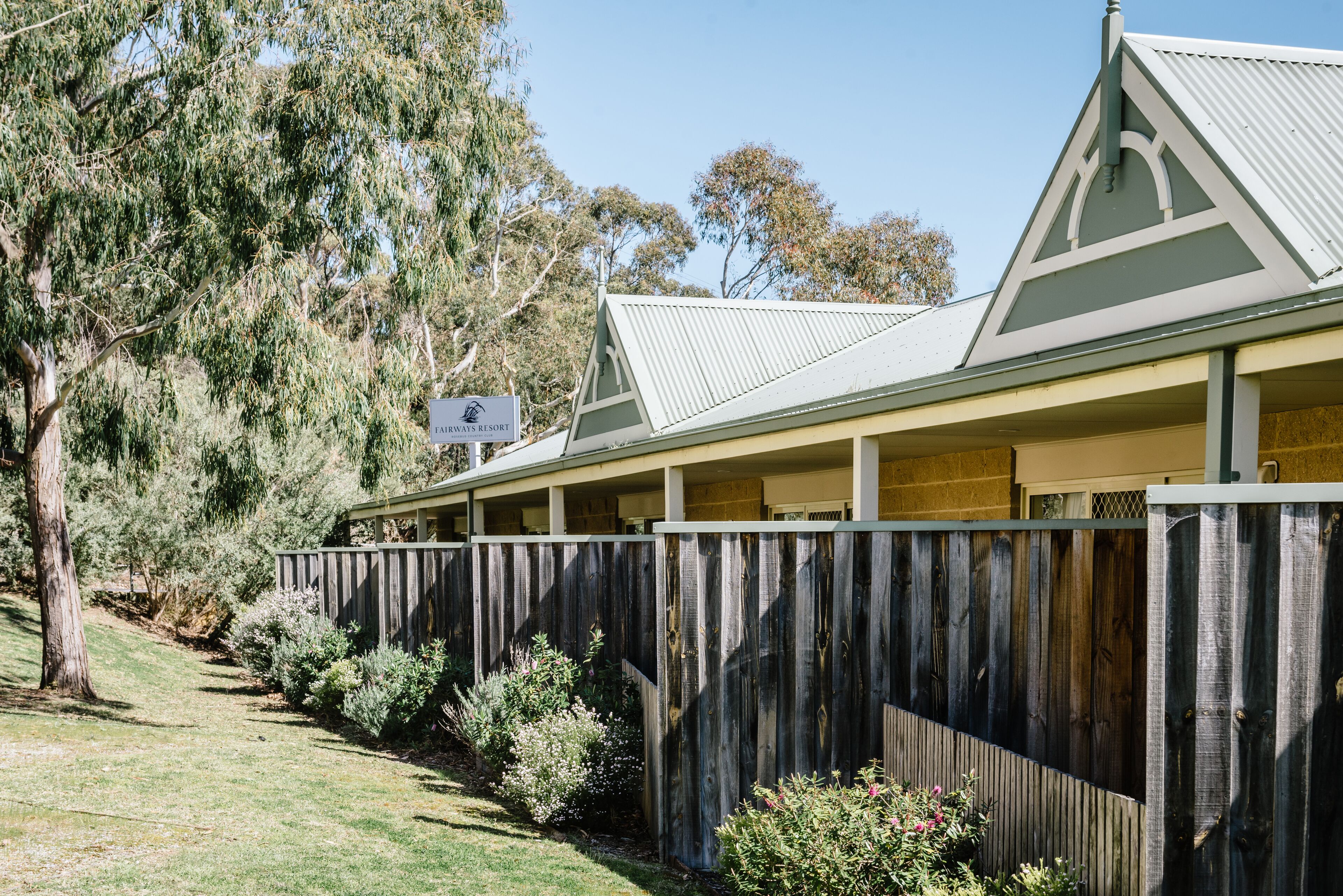 A row of rooms with a wooden fence, a sign for EAYWAYS RESORT, and a tree-lined pathway.