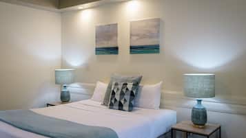 A neatly made bed with a blue blanket, two matching lamps, and two paintings on the wall.