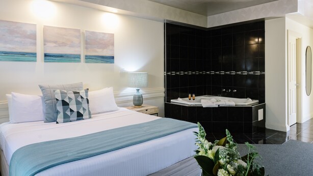 A modern hotel room with a large bed, a black bathtub, and three wall-mounted paintings. - Fairways Resort (Rosebud)