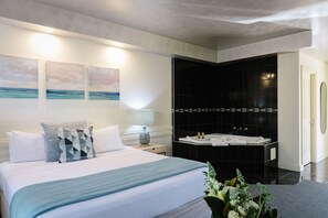 Una habitación de hotel moderna con una cama grande, una bañera negra y tres cuadros colgados en la pared.