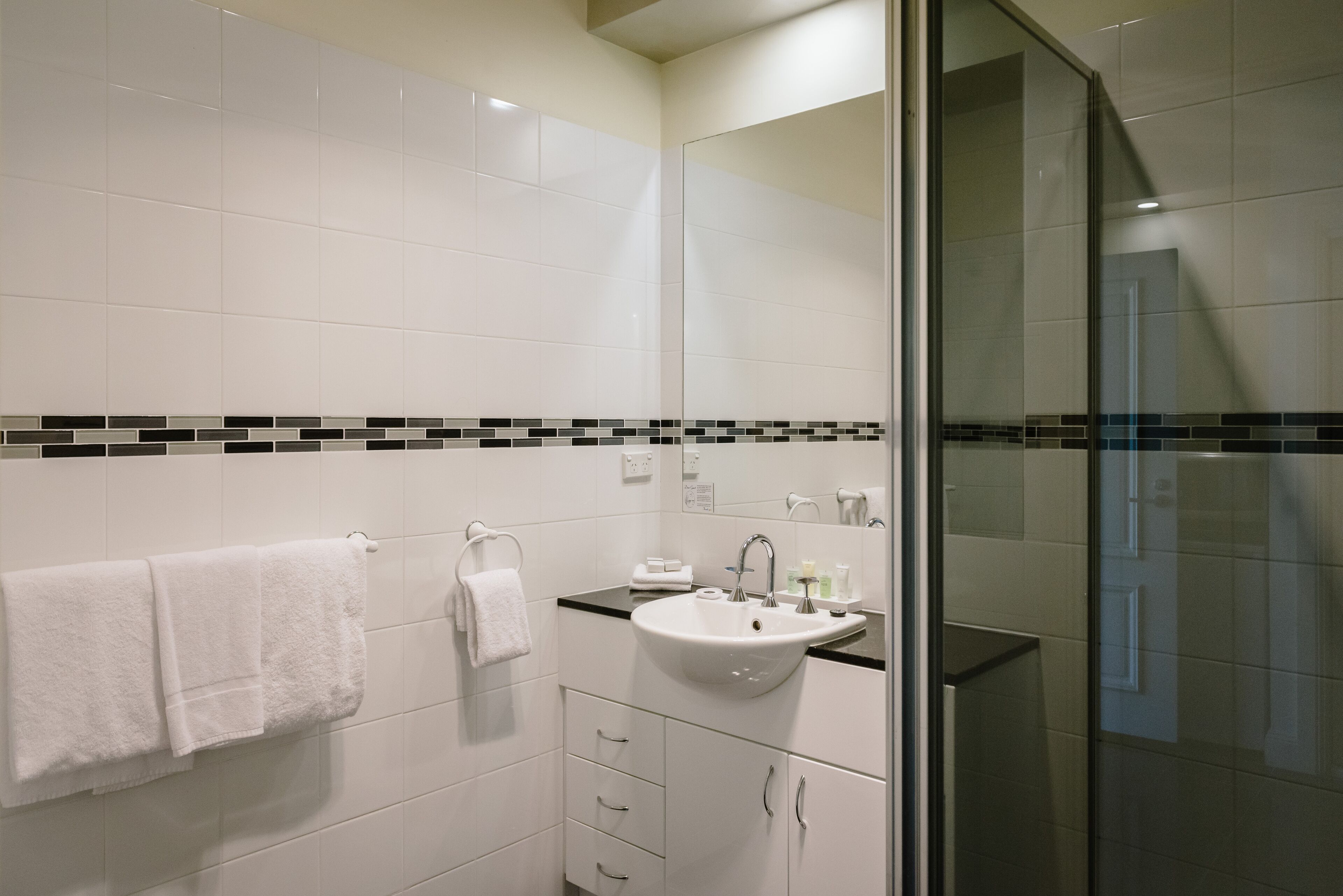 Un baño moderno con un lavabo blanco, encimera negra y cabina de ducha con mampara de vidrio.