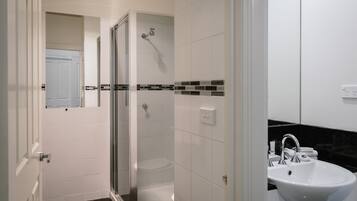Un baño con ducha de vidrio, azulejos blancos, encimera negra y lavamanos blanco.
