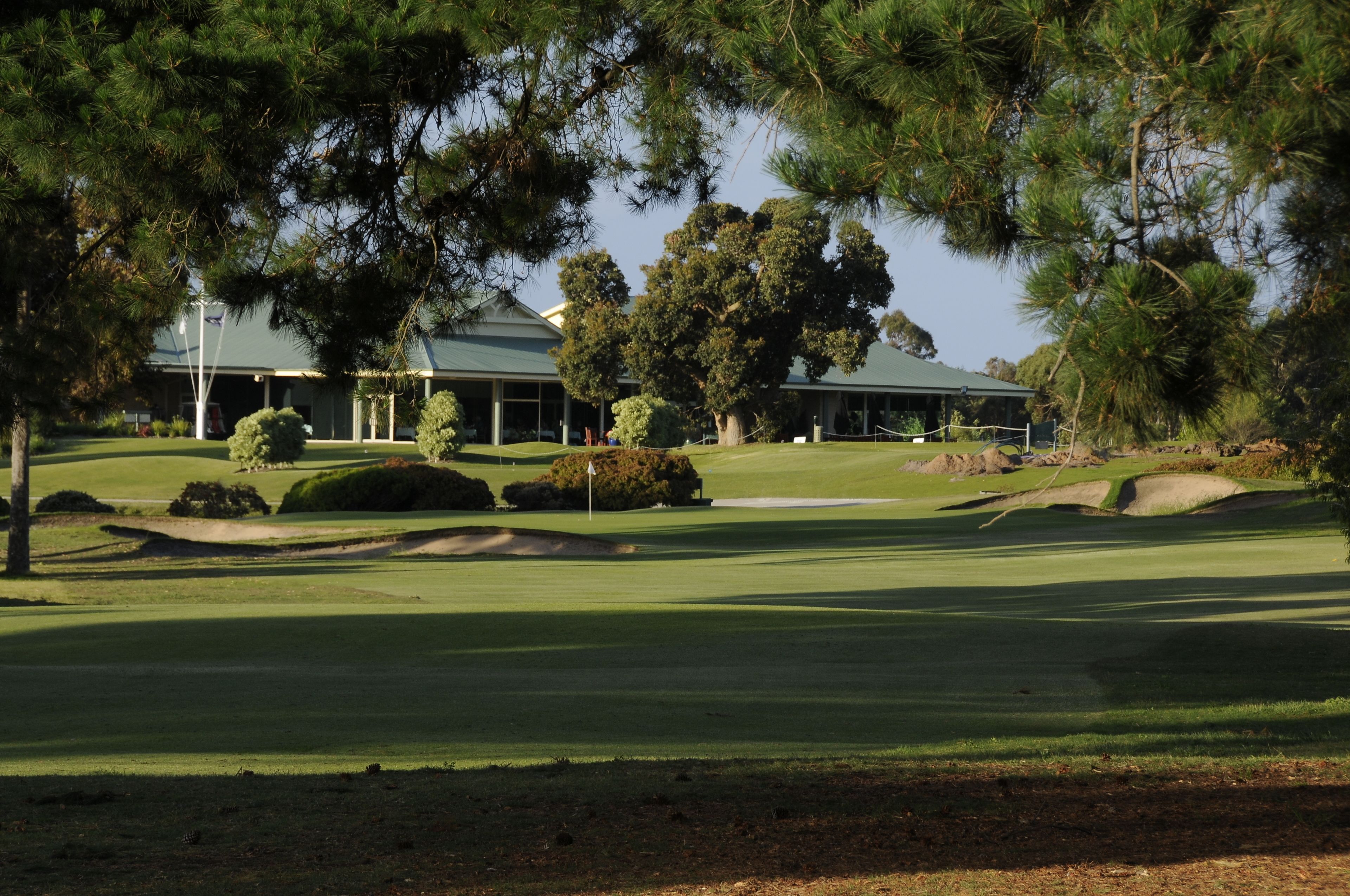 A golf course with a clubhouse, surrounded by trees and sand bunkers.
