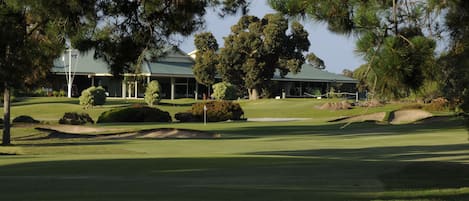 Ein Golfplatz mit Clubhaus, umgeben von Bäumen und Sandbunkern.