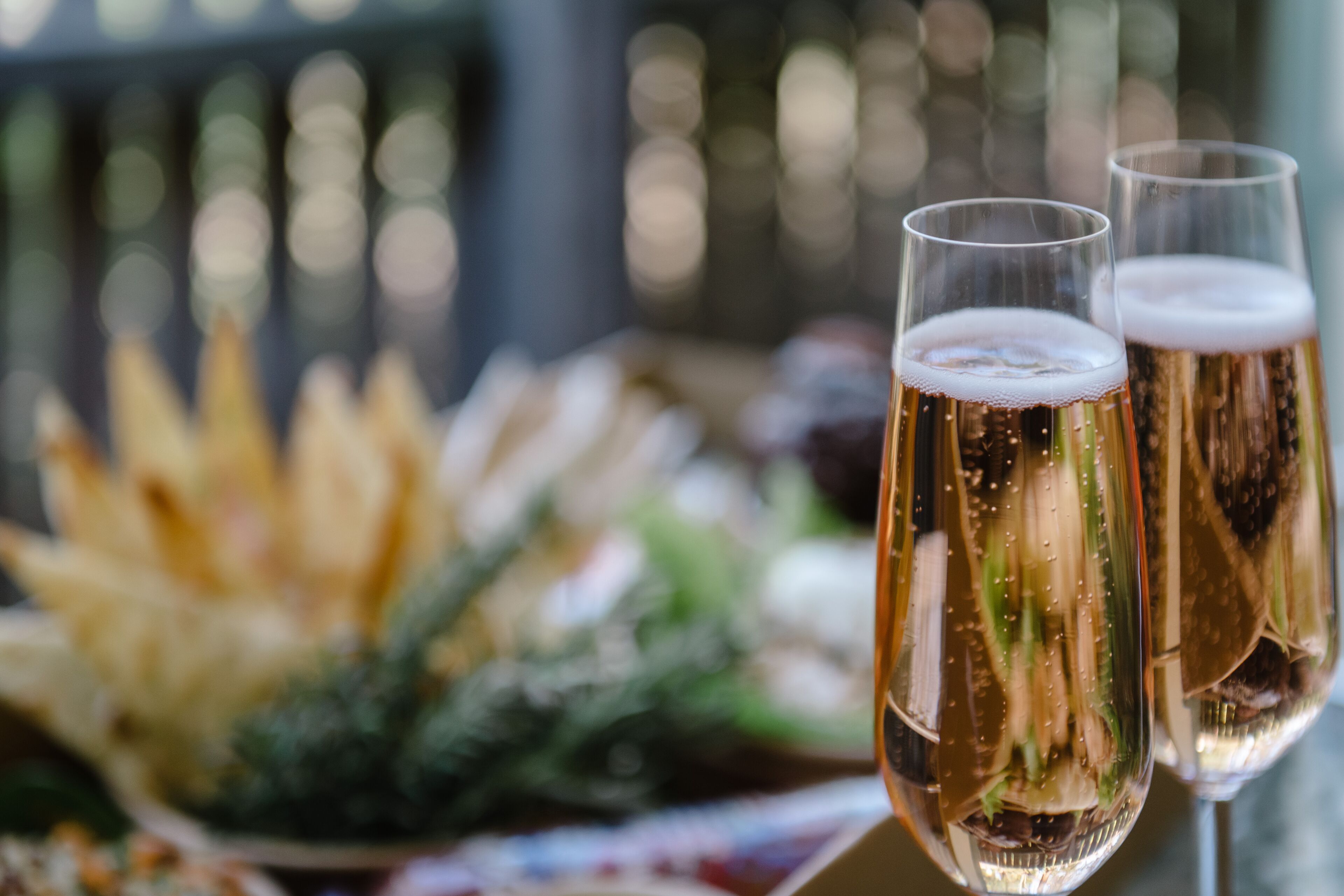 Deux coupes de champagne, avec un arrière-plan flou de verdure et une rambarde.